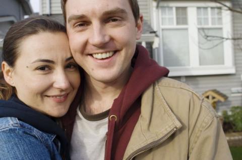 man and woman with arms around each other smiling in front of house