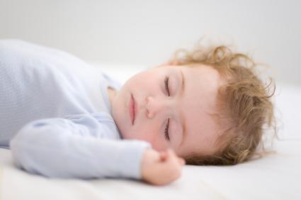 toddler sleeping on his back on bed