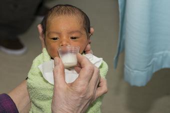 baby being fed, drinking milk out of a tiny plastic glass