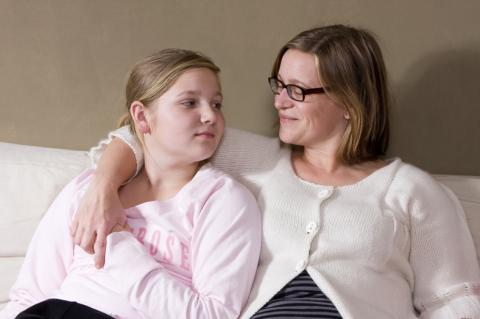 mom with arm around daughter on couch talking